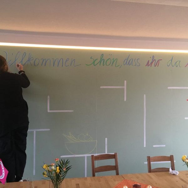 Wiedereröffnung: Das „MüZeL“ begrüßt seine Besucher*innen am neuen Standort - Mütterzentrum e.V. Leipzig Eine Frau schreibt an eine Wandtafel "Willkommen, schön, dass ihr da seid!"