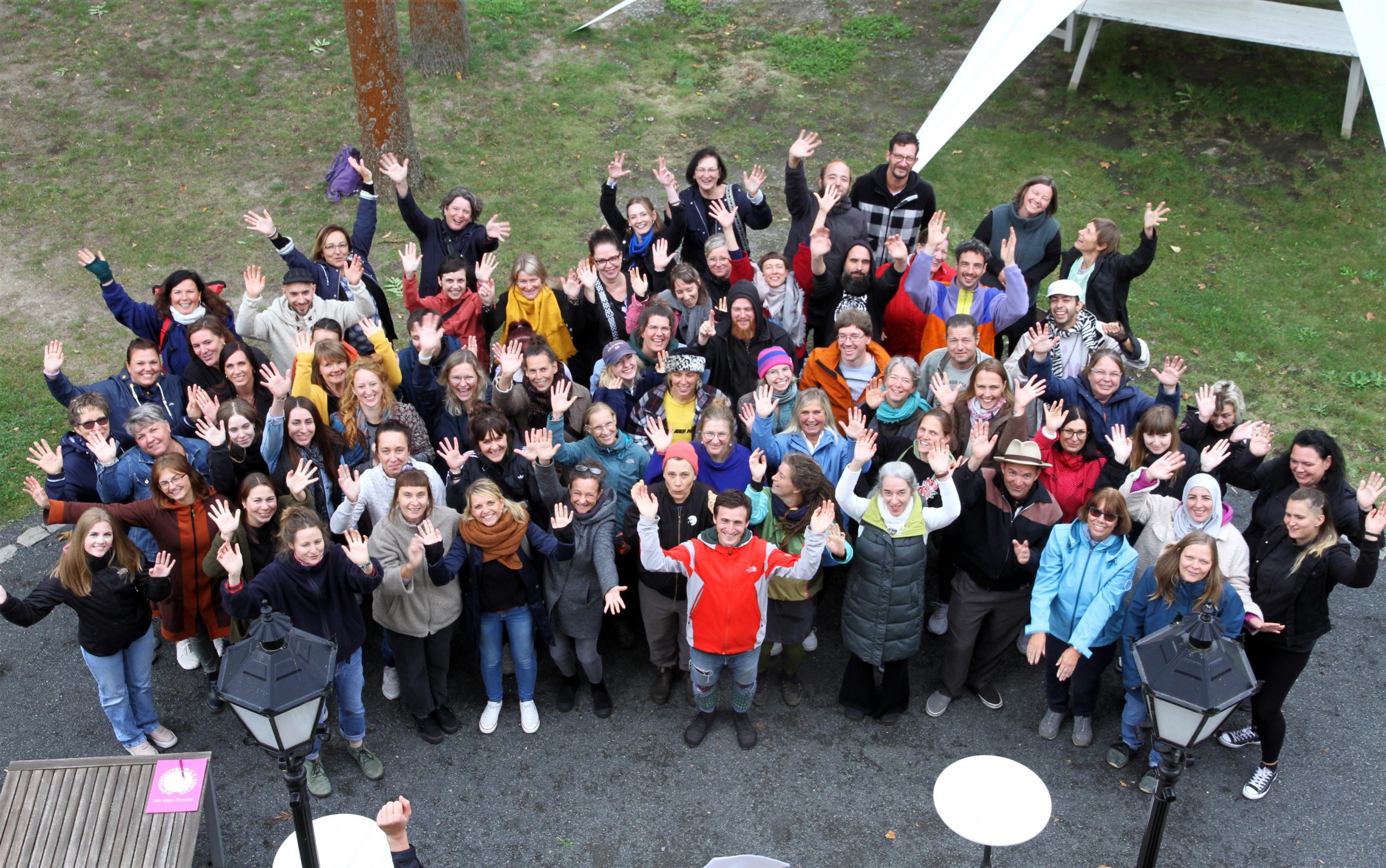 Ab 2026 heißt unser Verein FiZ Leipzig - Mütterzentrum e.V. Leipzig Ein Gruppenfoto der Mitarbeitenden des Mütterzentrum e.V. Leipzig, aufgenommen aus der Vogelperspektive: Personen unterschiedlichen Alters Lachen und Winken in die Kamera.