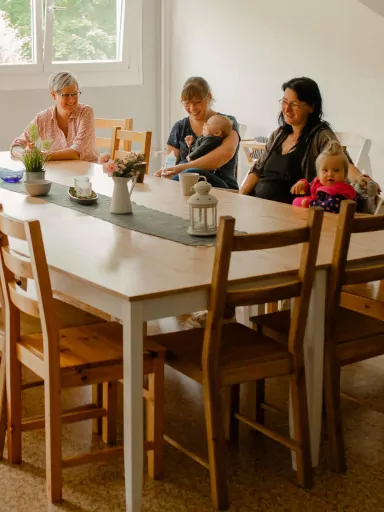 Frauen sitzen mit ihren Kindern am Tisch und lachen.