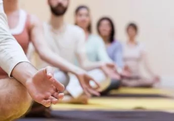 Personen sitzen in einer Reihe hintereinander auf Matten und meditieren.