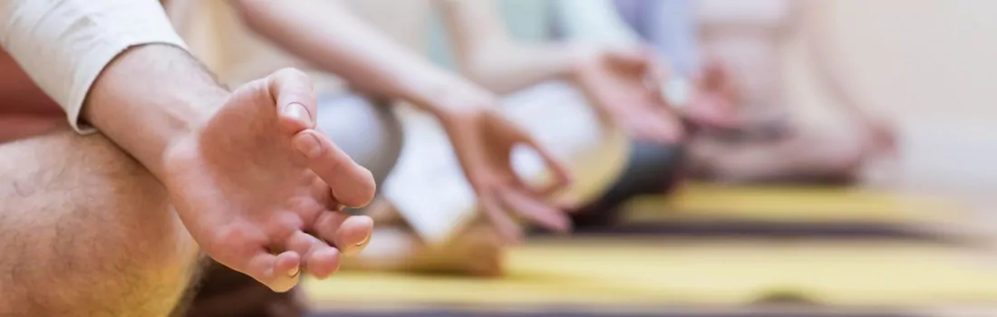 Personen sitzen in einer Reihe hintereinander auf Matten und meditieren.