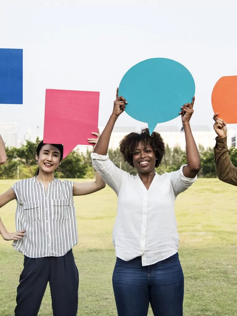 Personen, die eine Sprechblase hoch halten. Die Sprechblasen sind aus farbigen Papier ausgeschnitten.