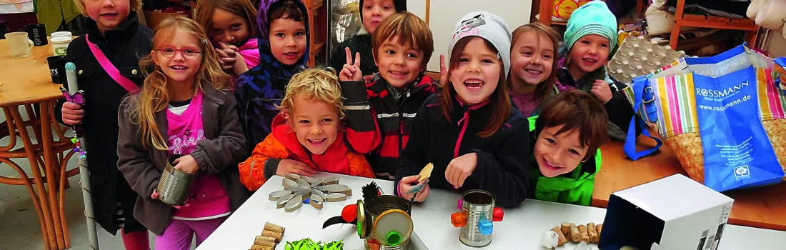 Viele Kinder stehen lächelnd hinter einem Tisch mit Upcycling-Gegenständen.