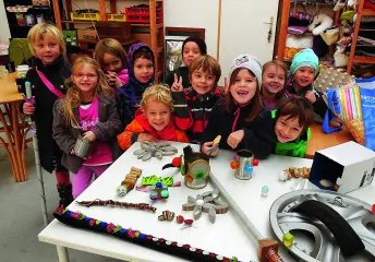 Viele Kinder stehen lächelnd hinter einem Tisch mit Upcycling-Gegenständen.
