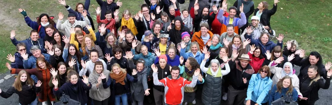 Ein Gruppenfoto der Mitarbeitenden des Mütterzentrum e.V. Leipzig, aufgenommen aus der Vogelperspektive: Personen unterschiedlichen Alters Lachen und Winken in die Kamera.